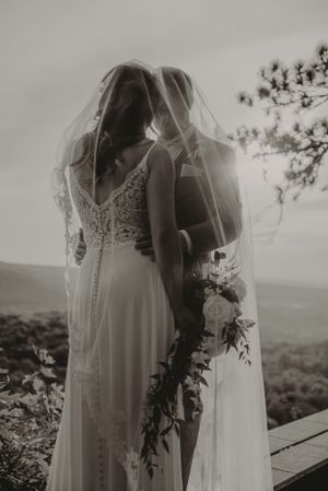 Artistic black and white wedding photo with veil flowing in mountain breeze.