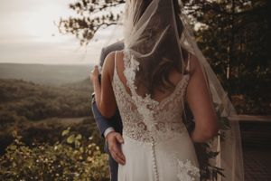 Back view of detailed lace wedding dress against sunset mountain scenery.