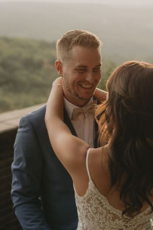 Intimate moment between couple in wedding attire on outdoor viewing platform with mountain backdrop.