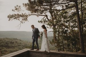 Couple walks along wooden deck overlooking vast mountain landscape.