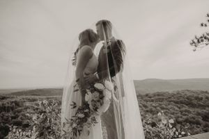Black and white romantic wedding moment with flowing veil against mountain backdrop.