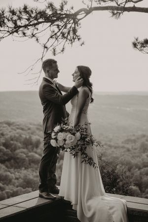 Black and white portrait of couple with bouquet against sweeping valley views.