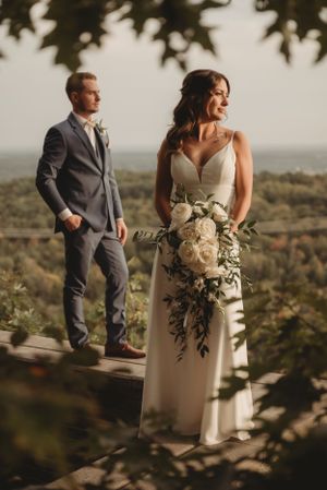 Elegant wedding couple on a mountaintop deck with dramatic landscape views and natural lighting.