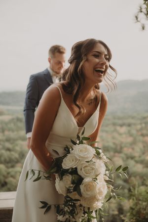 Candid moment of joy during a mountain-view wedding photoshoot with white roses bouquet.