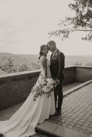 Black and white portrait of couple embracing on stone terrace with mountain views.