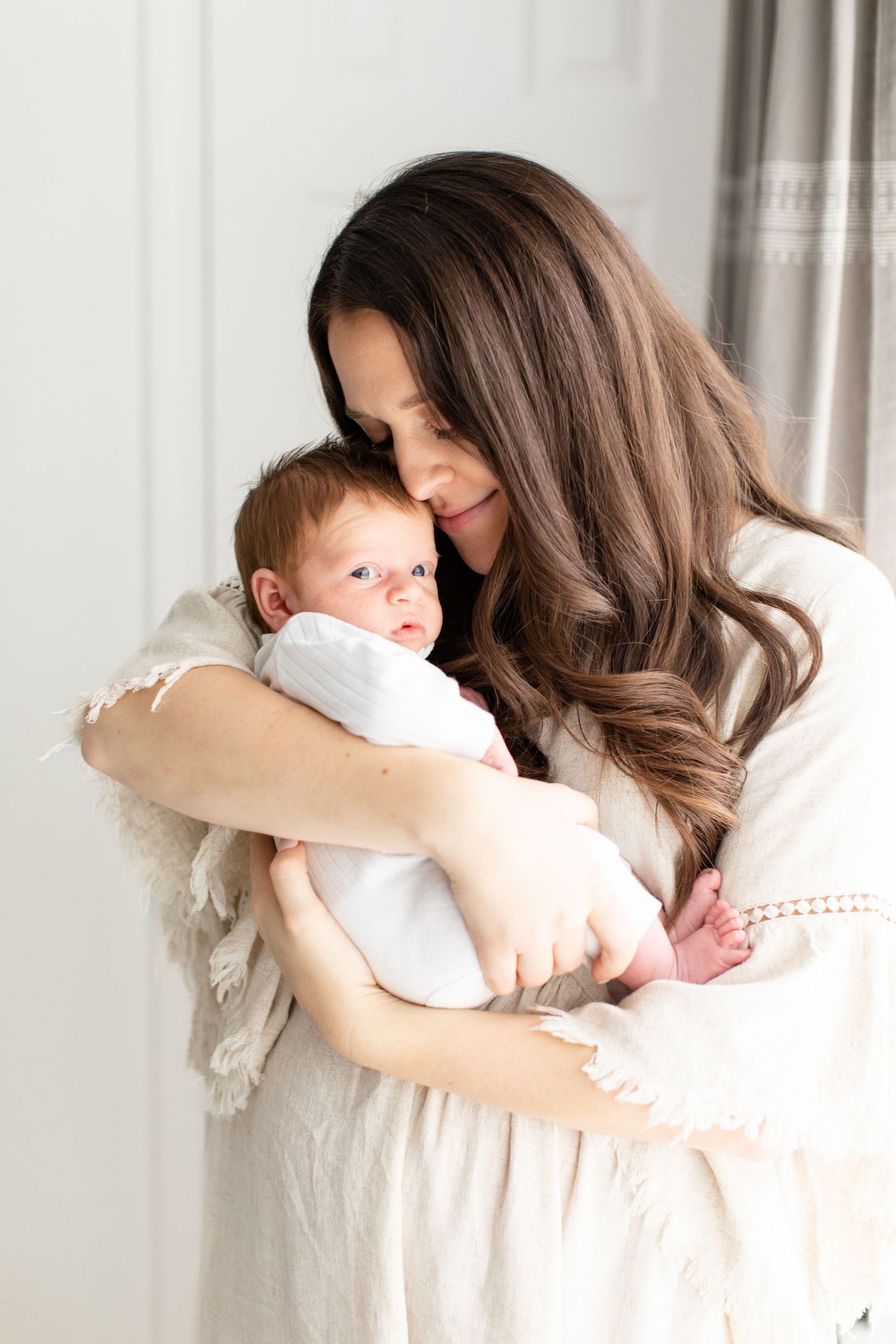 An intimate portrait showing gentle embrace between parent and baby in white clothing.