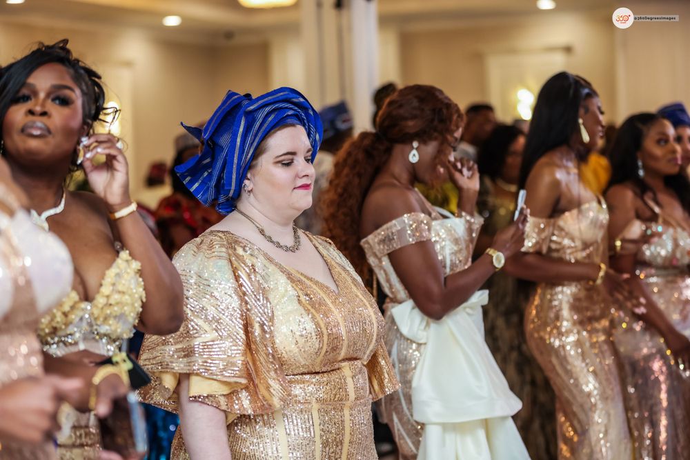 Women in gold sequin dresses and blue gele headwraps celebrate at a Nigerian traditional wedding ceremony.