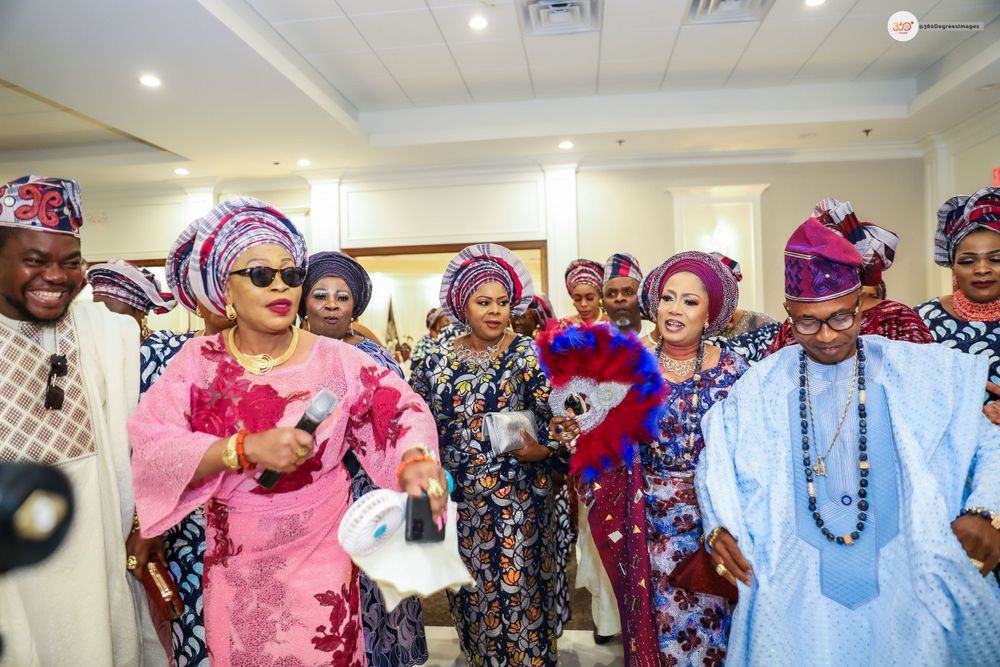 Elegantly dressed women in pink and blue aso-oke attire celebrate at a colorful Yoruba traditional wedding.