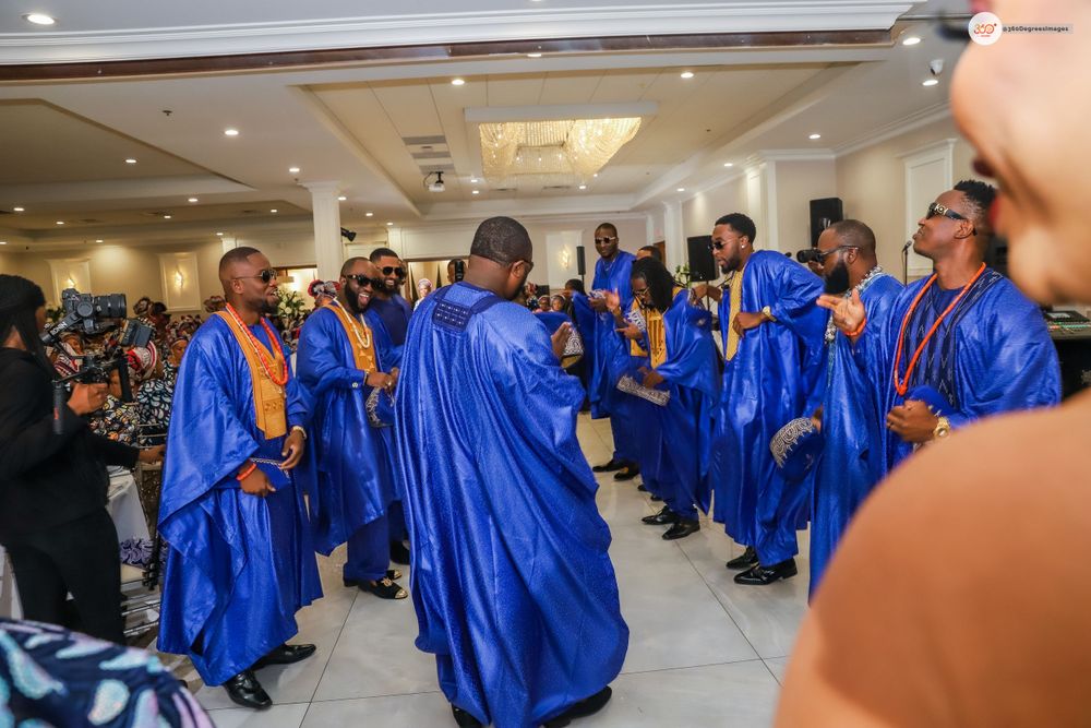 Men in royal blue agbada robes perform a traditional dance at a Nigerian wedding celebration.