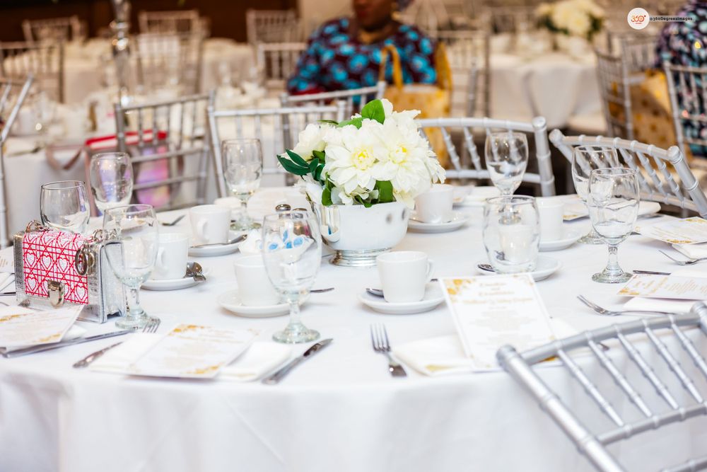 Elegant white wedding reception table setting with floral centerpiece and Chiavari chairs.