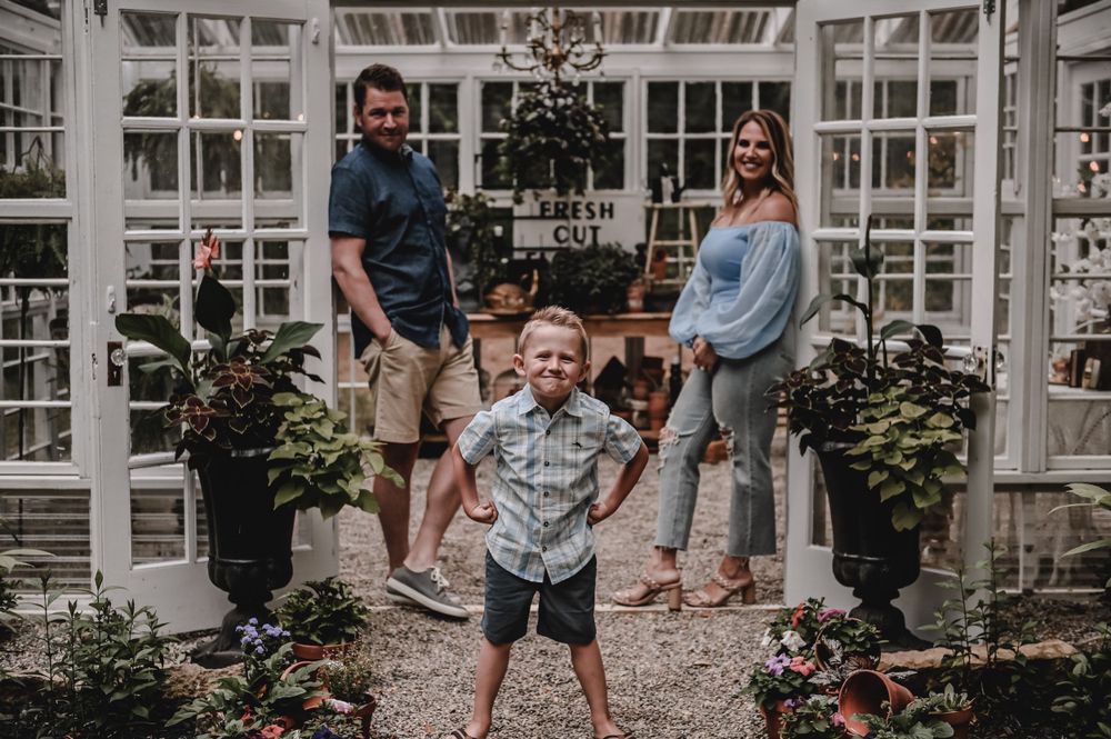 Family photo in a greenhouse with excited child jumping in the foreground.