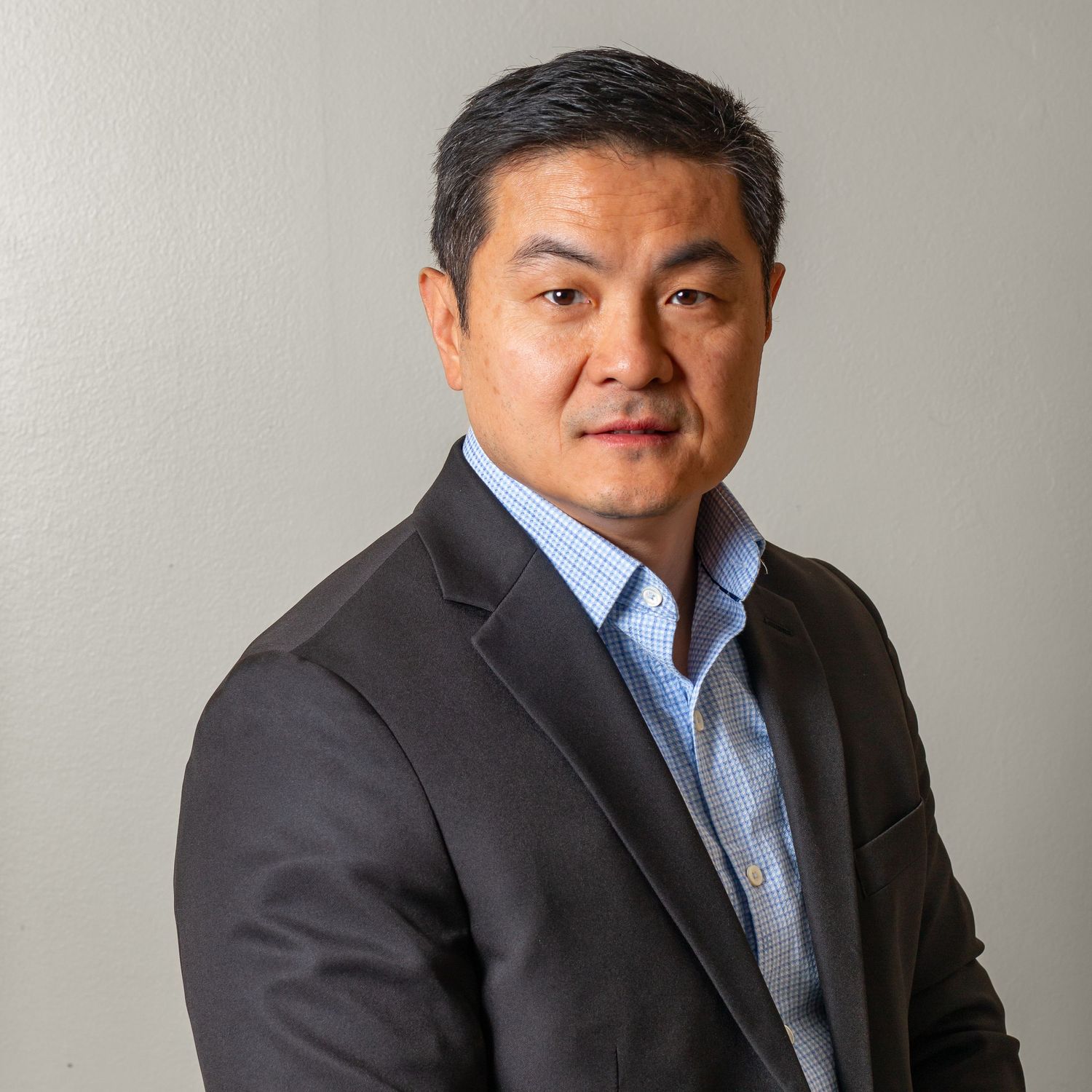 Professional business headshots of a person in a dark suit and blue shirt against a gray background.