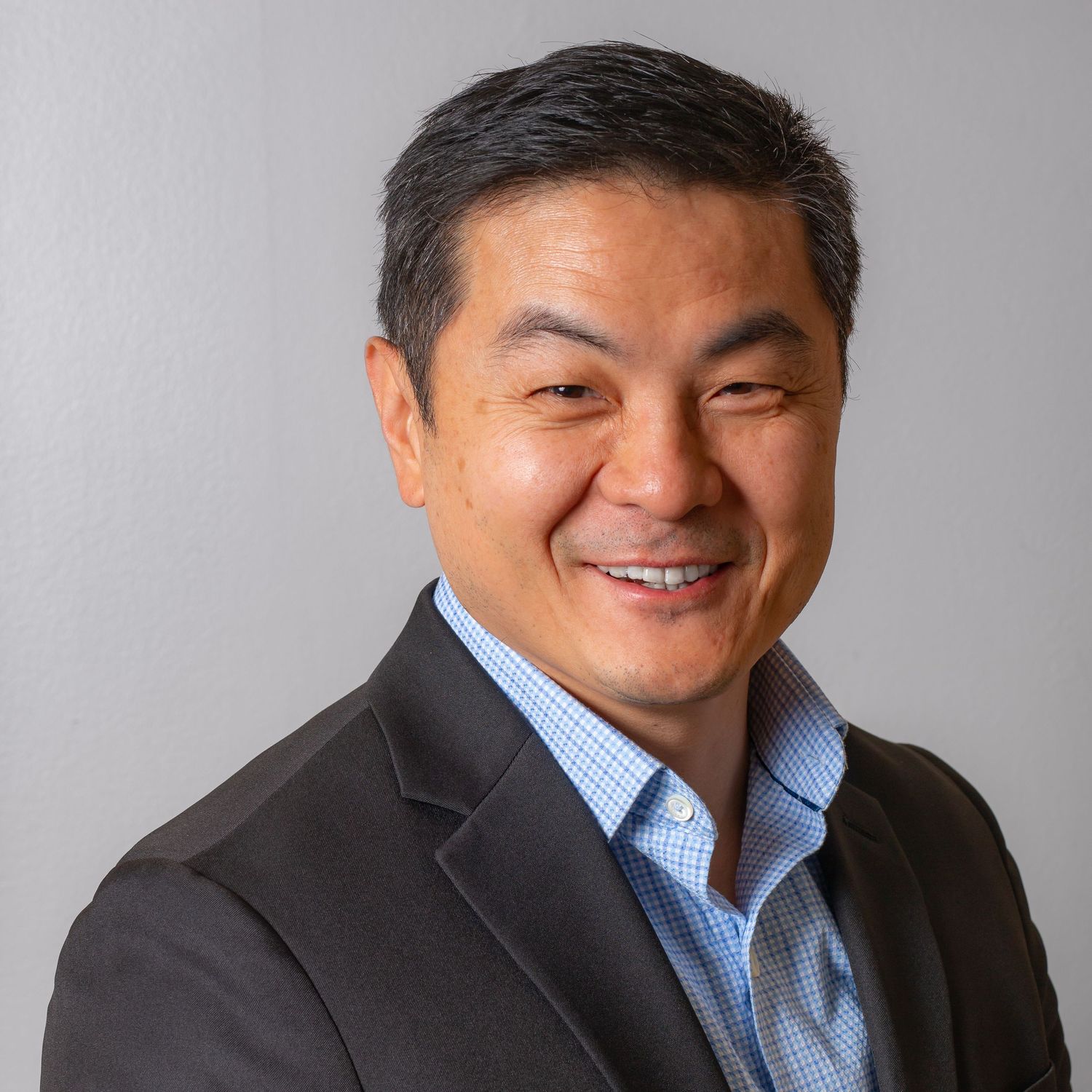 Professional headshots in business attire against grey background showing friendly expressions.