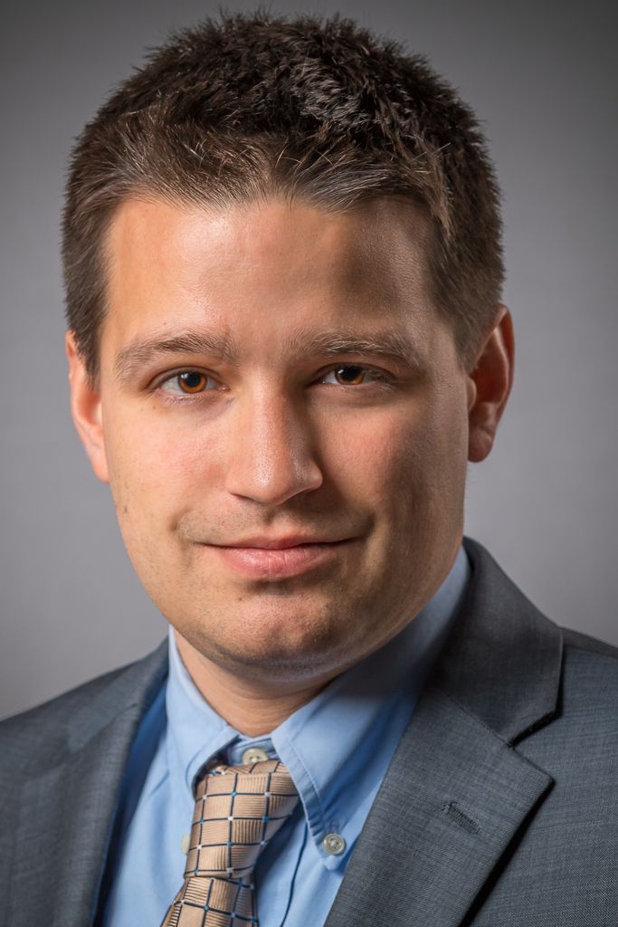 Professional headshot series of person in business suit with varied expressions against grey background.
