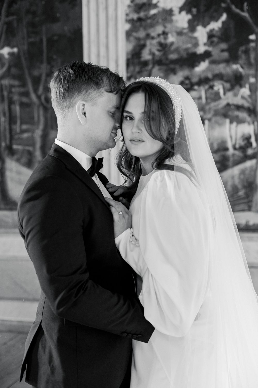 An intimate black and white portrait of newlyweds in front of a decorative mural.