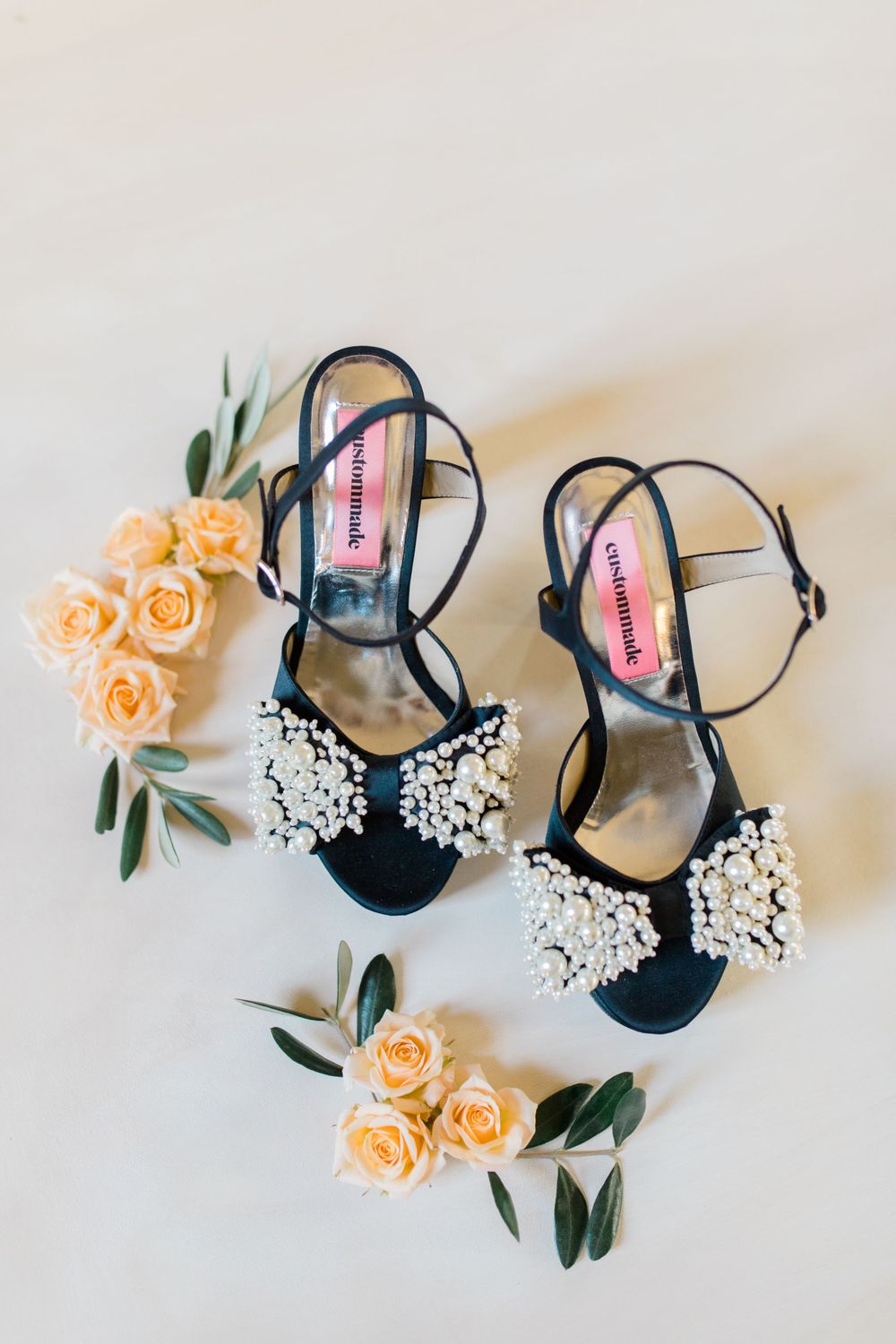 Pearl-embellished black wedding sandals with peach roses and greenery.