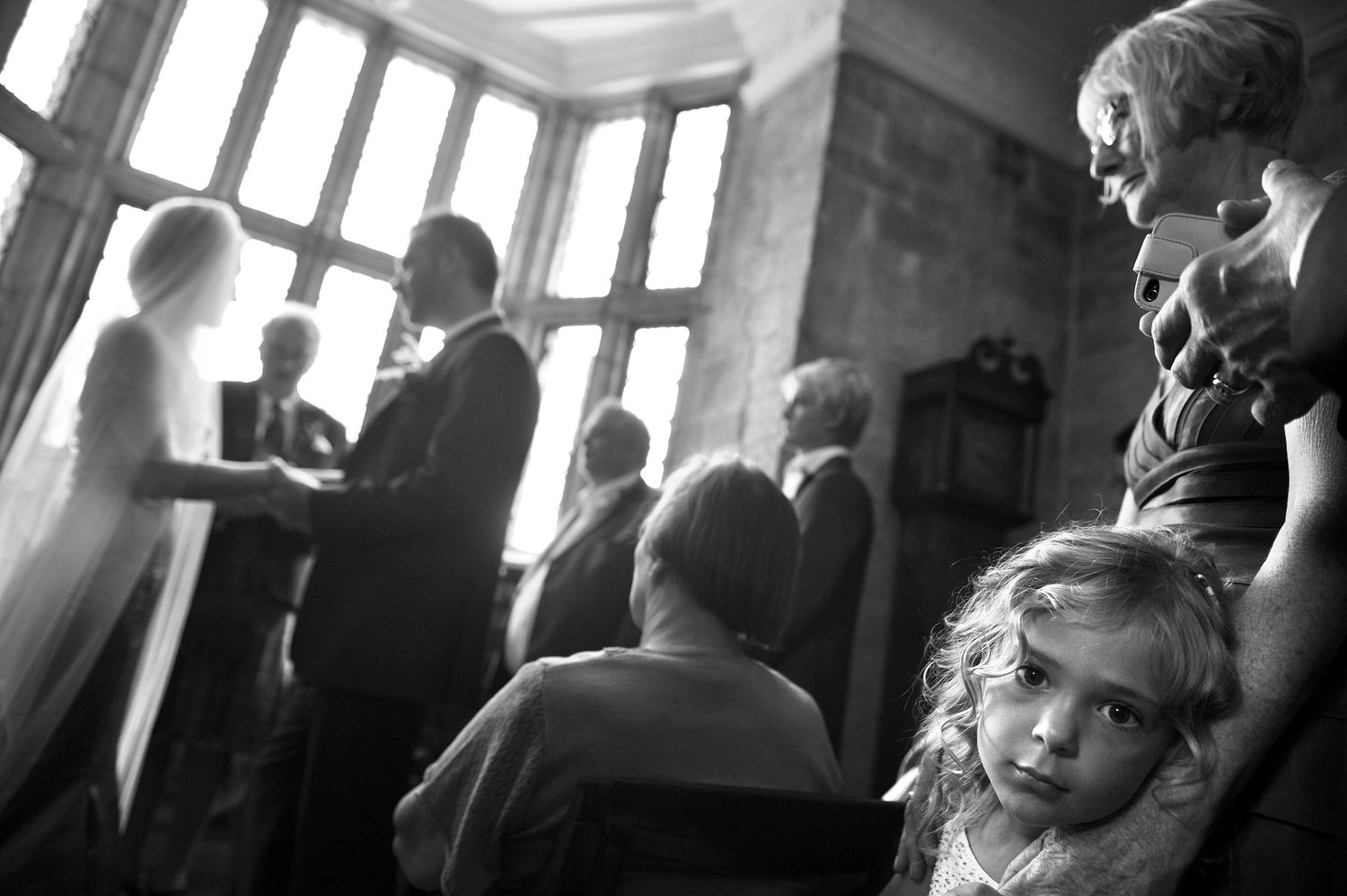 flower girl looks at the camera while a wedding takes place in the background