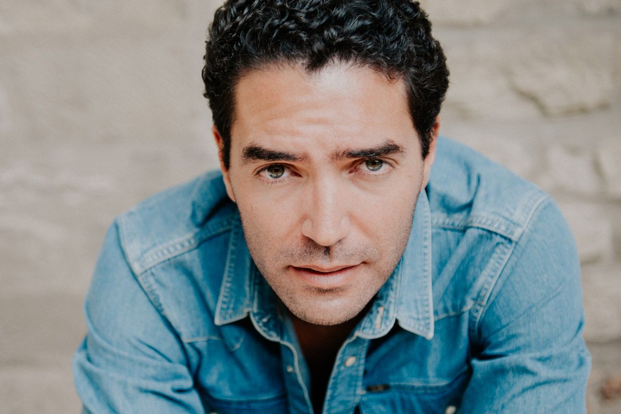 Portrait in casual denim against neutral background with warm lighting.