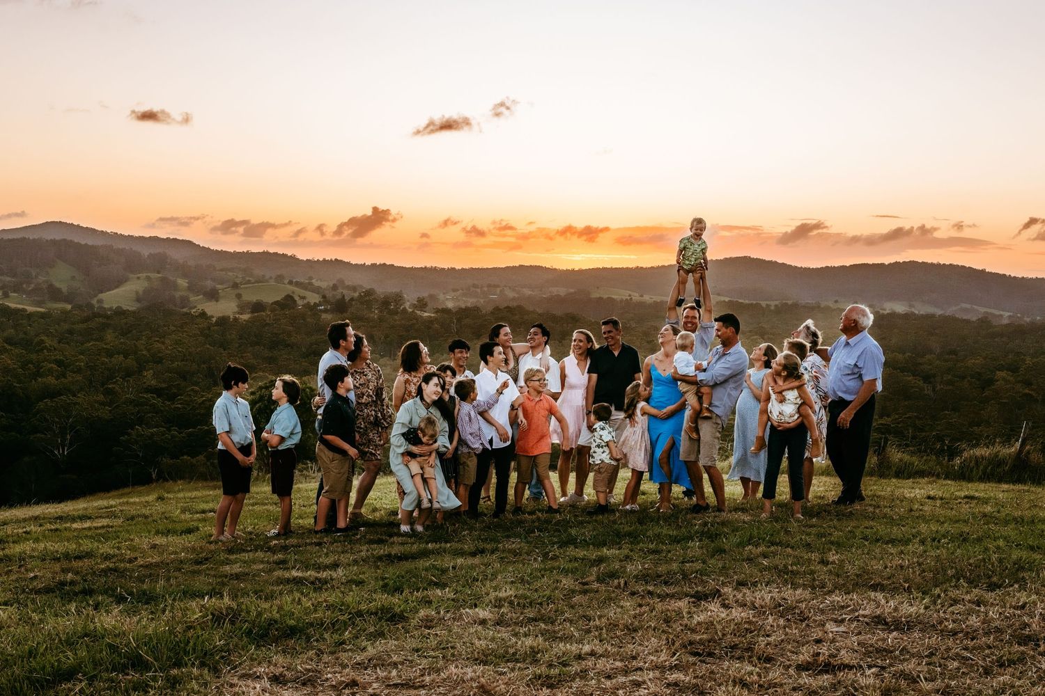 Large group gathered on hillside during sunset with mountains in background.