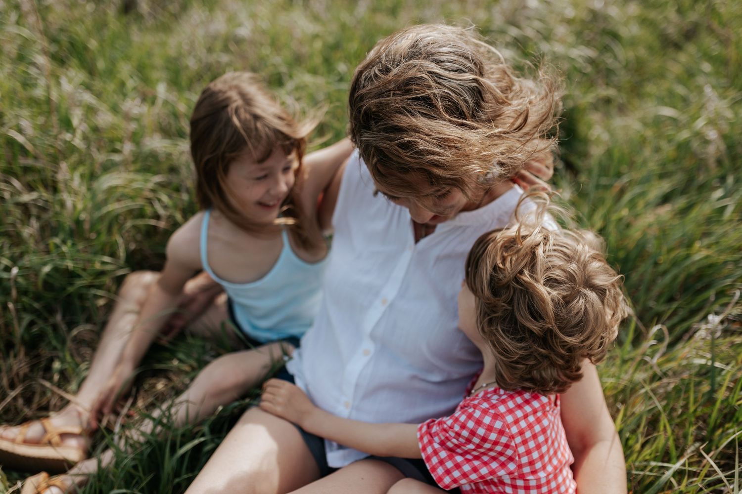 A mom smiles with her two young daughters as they sit in a tallgrass field for a family photo in Overland Park, KS.