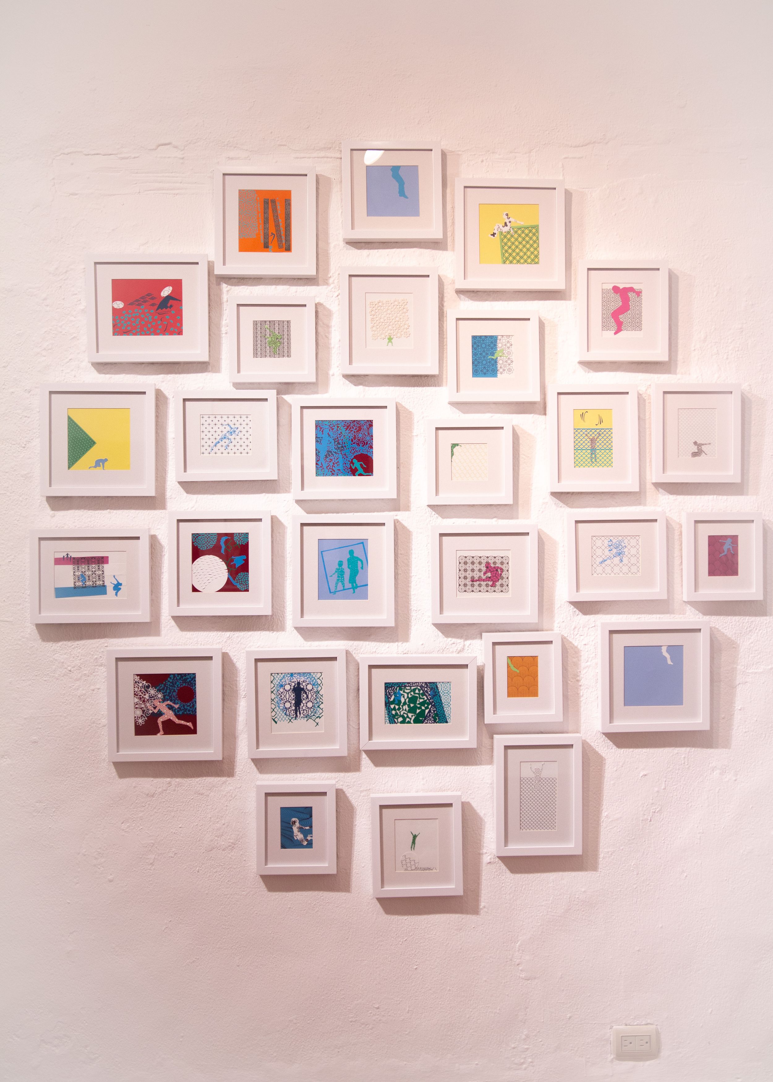 Gallery wall arrangement of small framed artworks in geometric pattern on white wall.