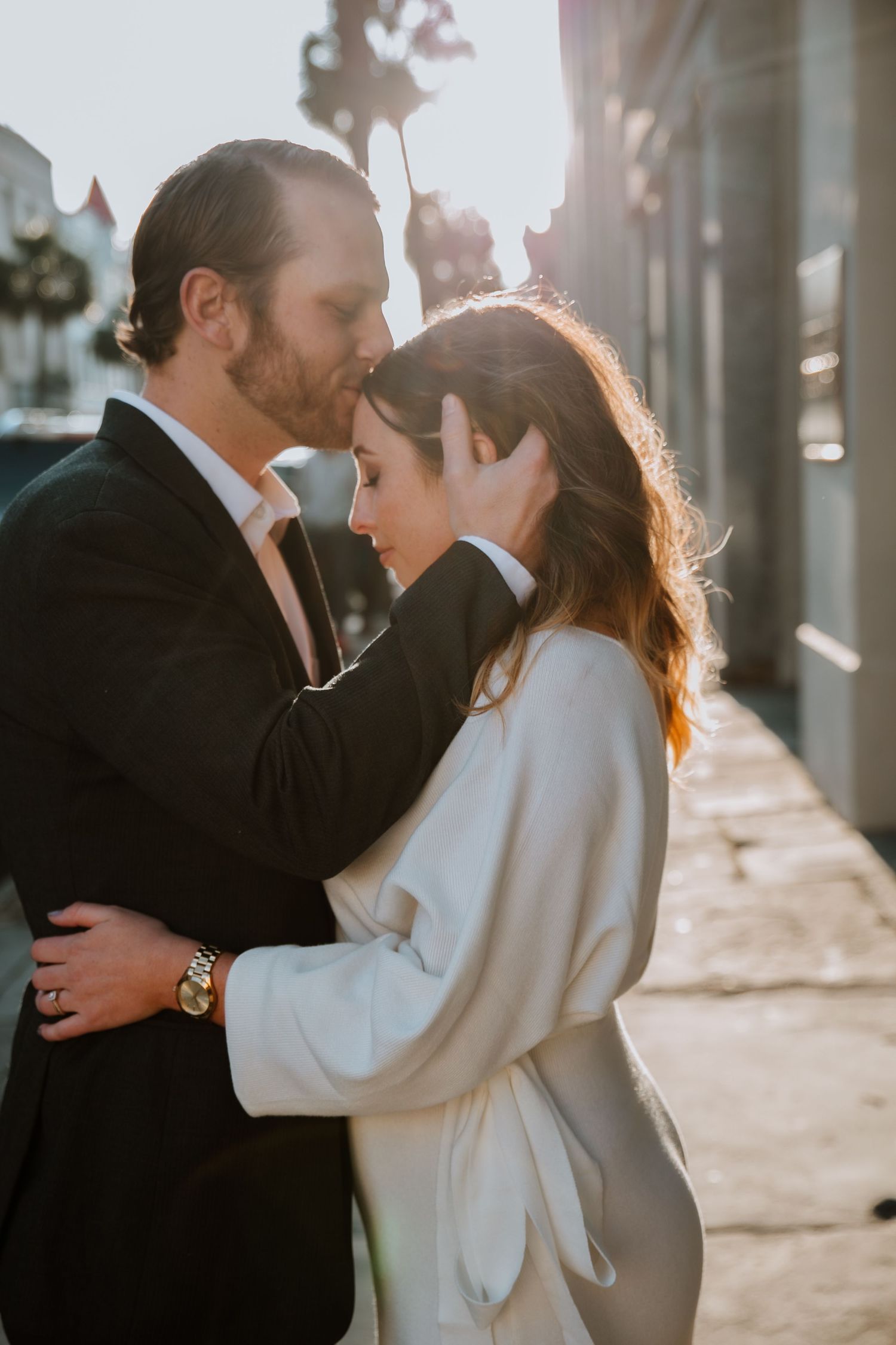 A man kisses his fiancé on her head while she looks serene