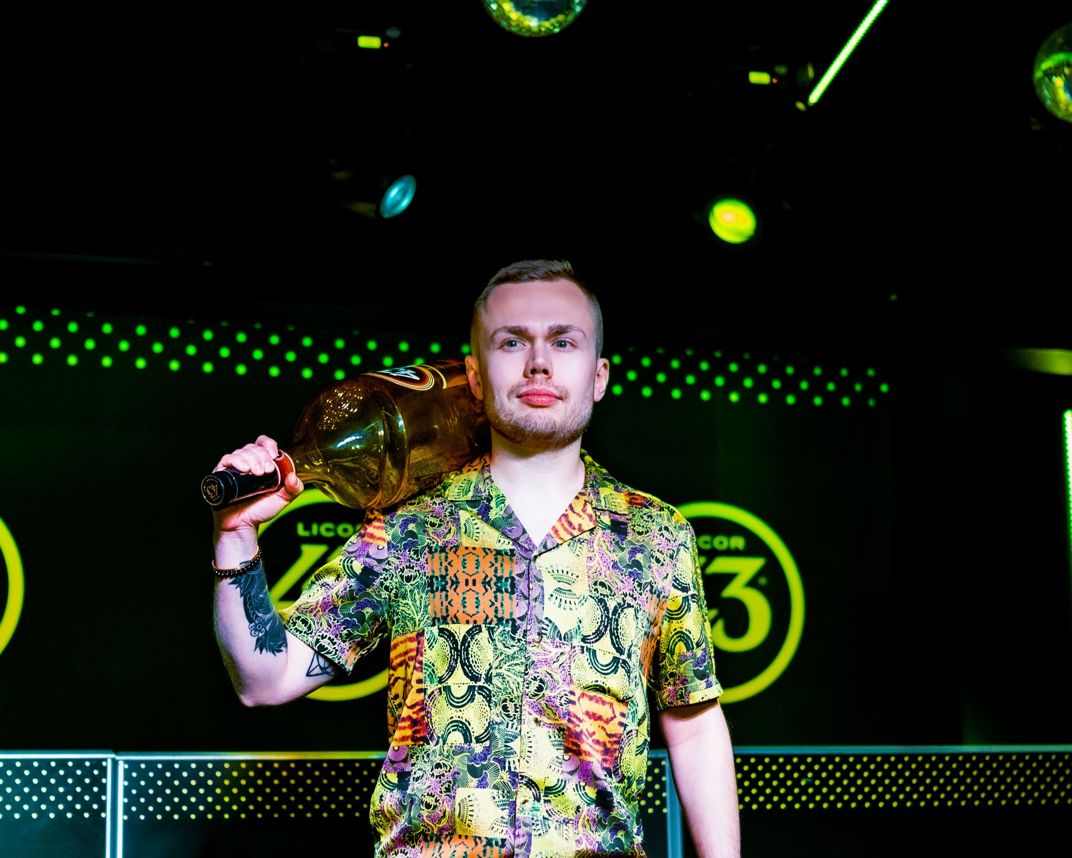 Person in floral shirt holds bottle while posing in front of Licor 43 logo display.