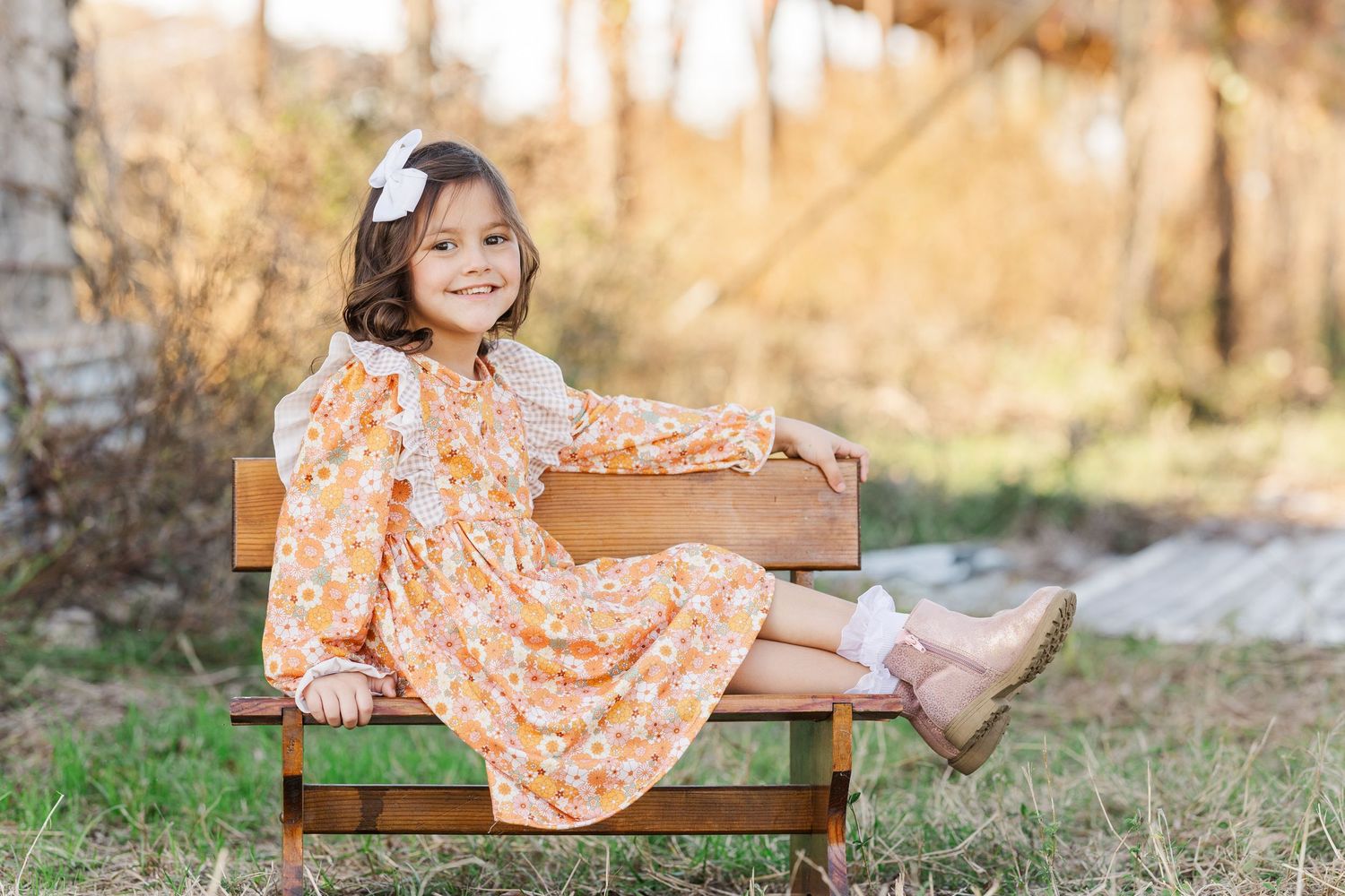 Young girl in peach dress sitting on wooden bench holding decorative box outdoors.