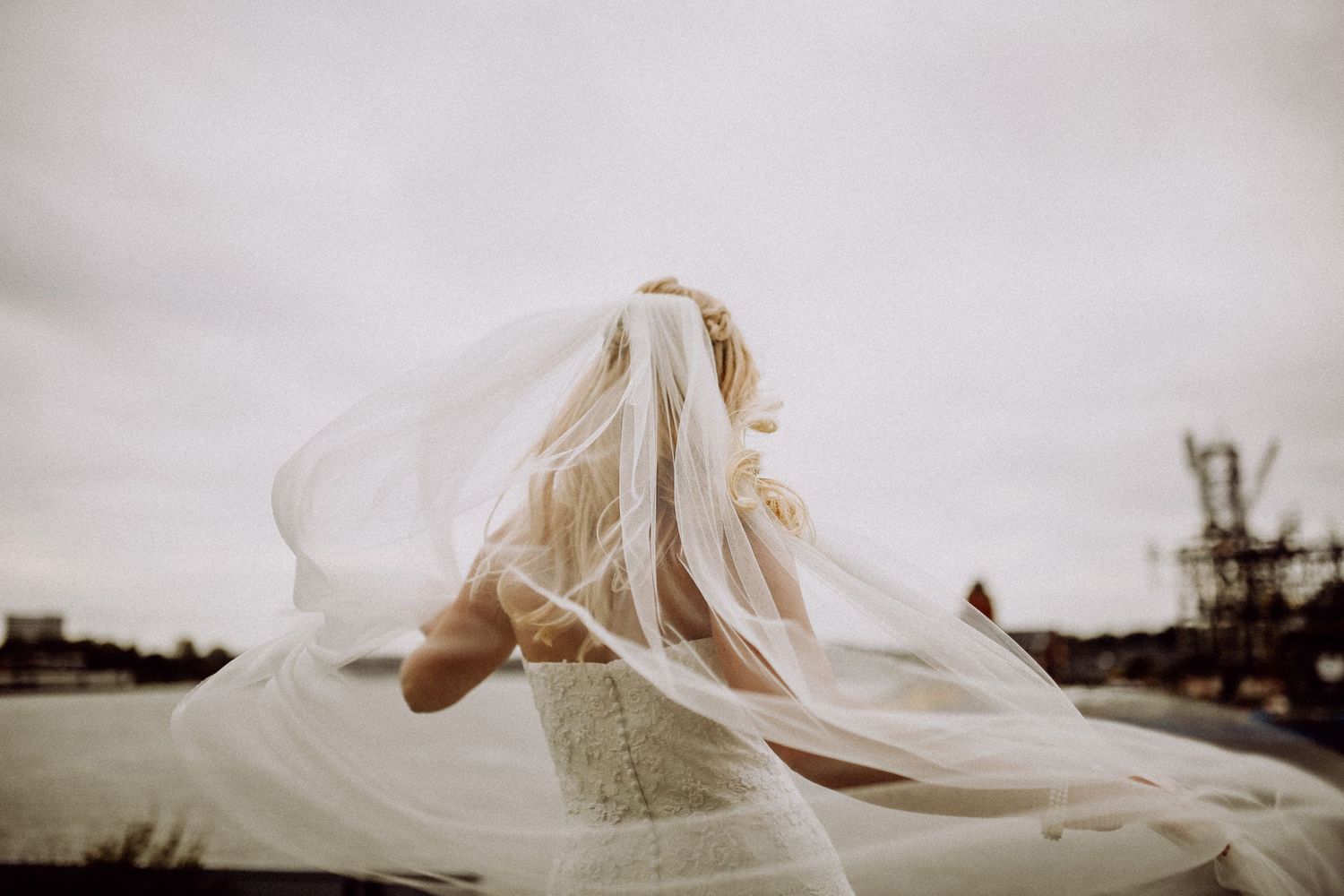 A wedding veil billows dramatically in the wind against an overcast sky, creating an ethereal and romantic moment.