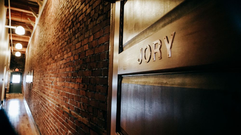 Dark hallway with exposed brick wall and wooden door labeled Jory.