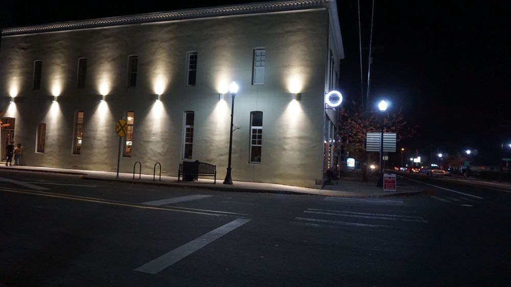 Night view of an illuminated brick building with dramatic uplighting on an urban street corner.