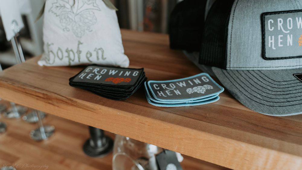 Baseball caps and patches displayed on a wooden shelf with Crown Hen branding.