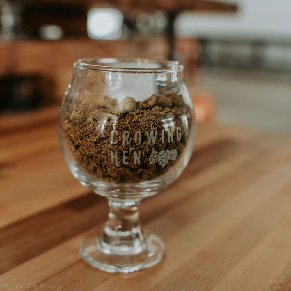 Empty glass goblet with Crown Brewing logo sitting on wooden surface.