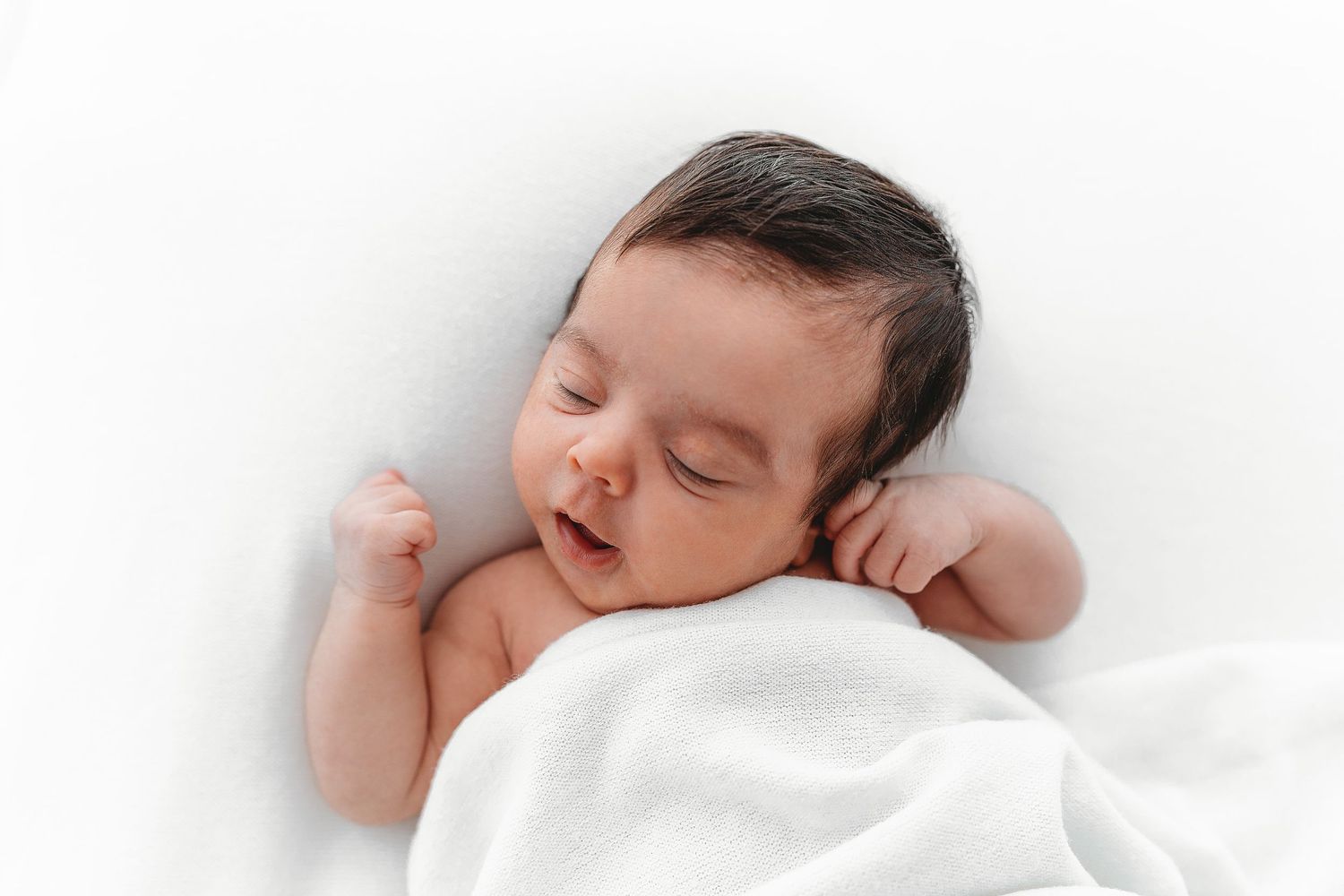 Peaceful sleeping baby wrapped in soft white blanket during newborn photoshoot.