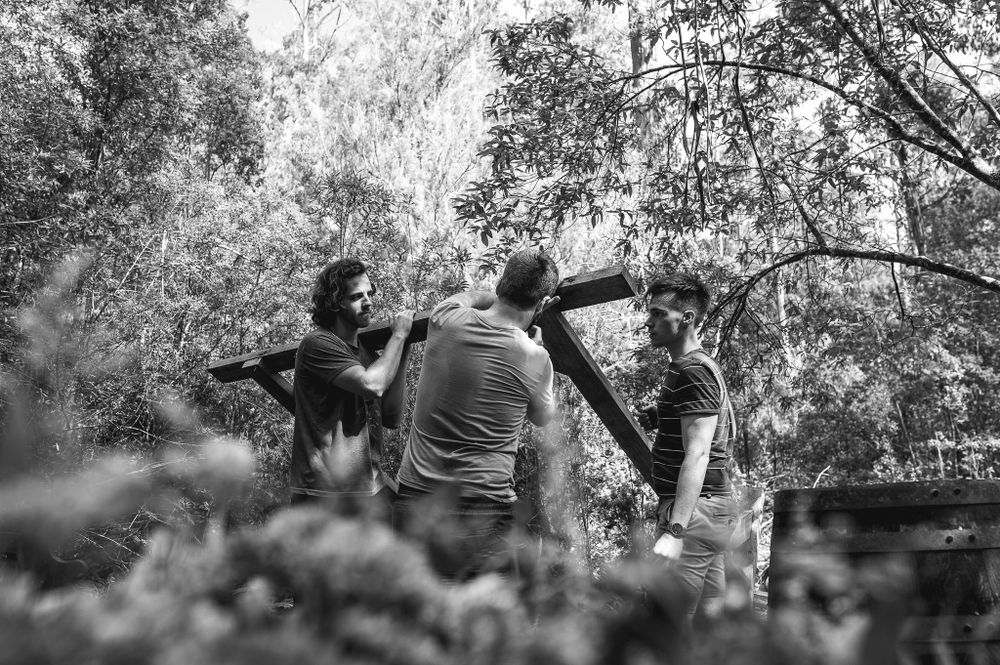 Group of people working together on an outdoor construction project in a wooded area.