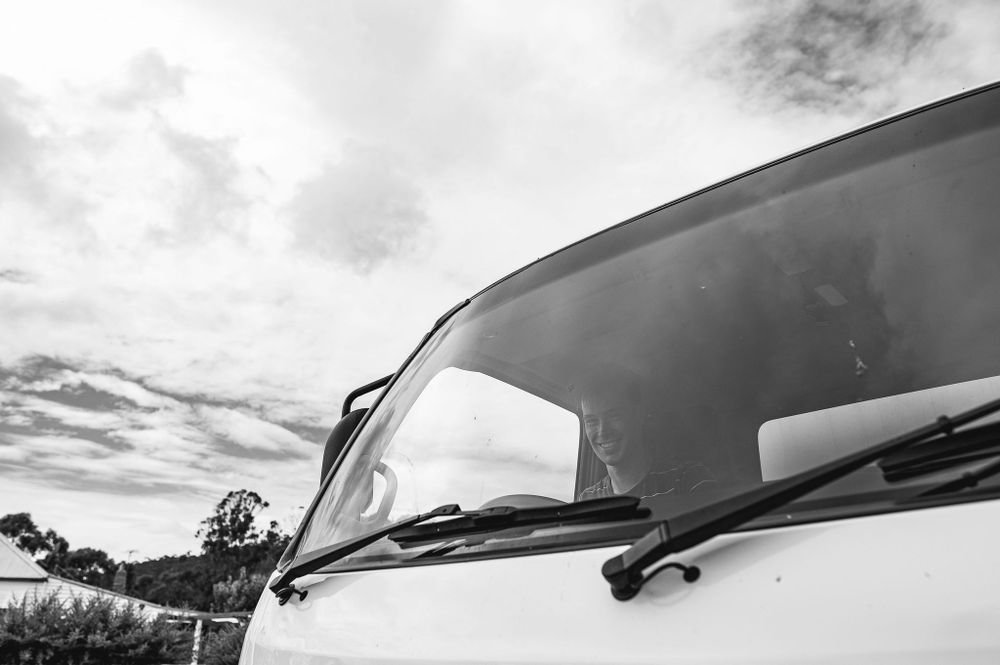 Black and white view of a vintage car windshield against a cloudy sky.