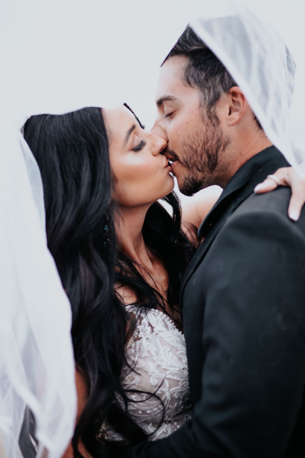 A romantic wedding kiss captured under a flowing white veil.