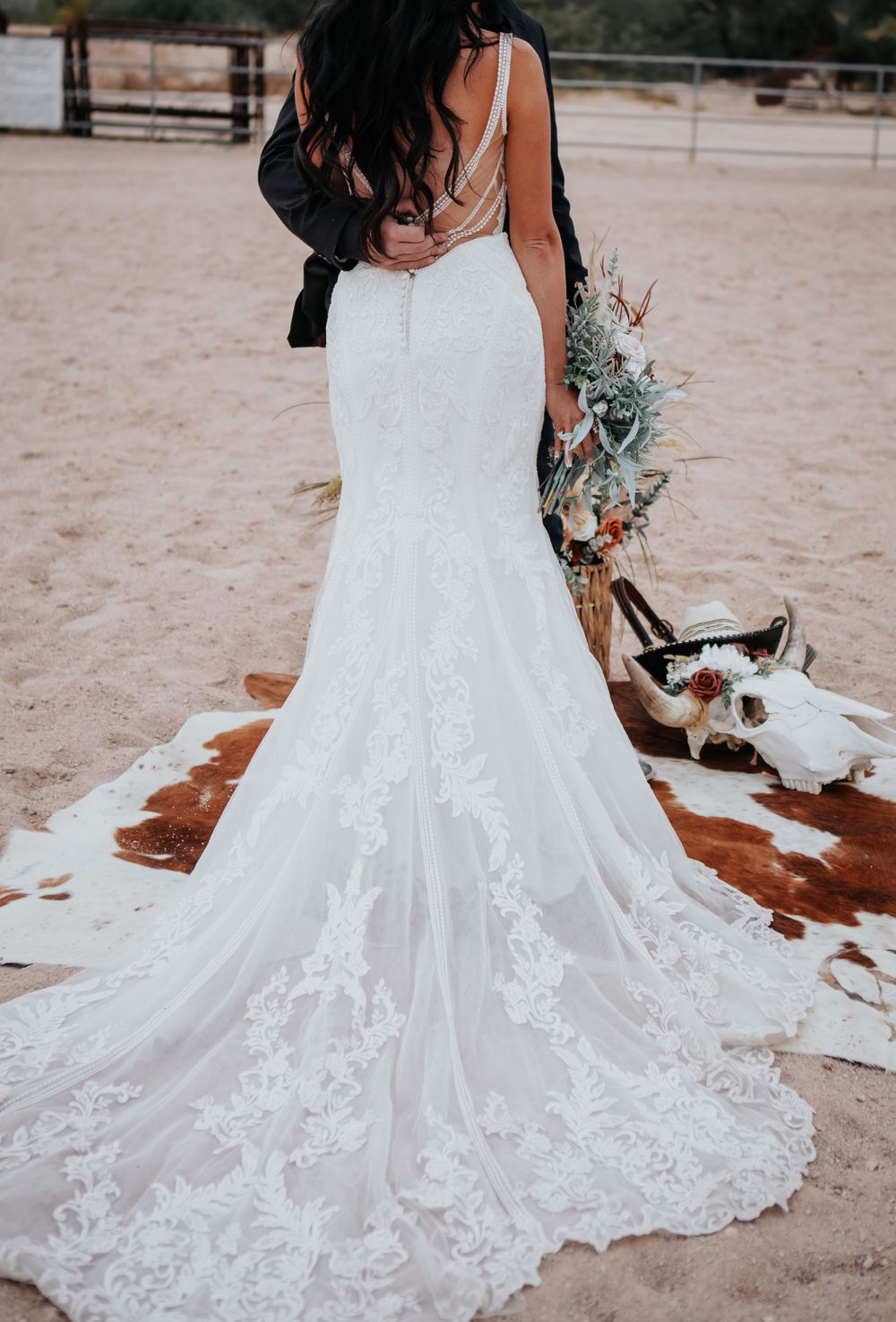 A detailed lace wedding dress train spreads across sandy ground.