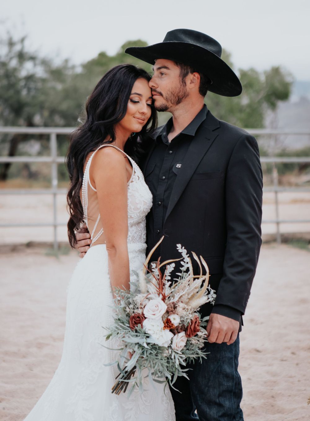 A western-style wedding couple poses with rustic bouquet in desert setting.