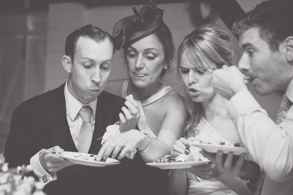 Wedding guests blow on their hot food at a reception dinner table in black and white.