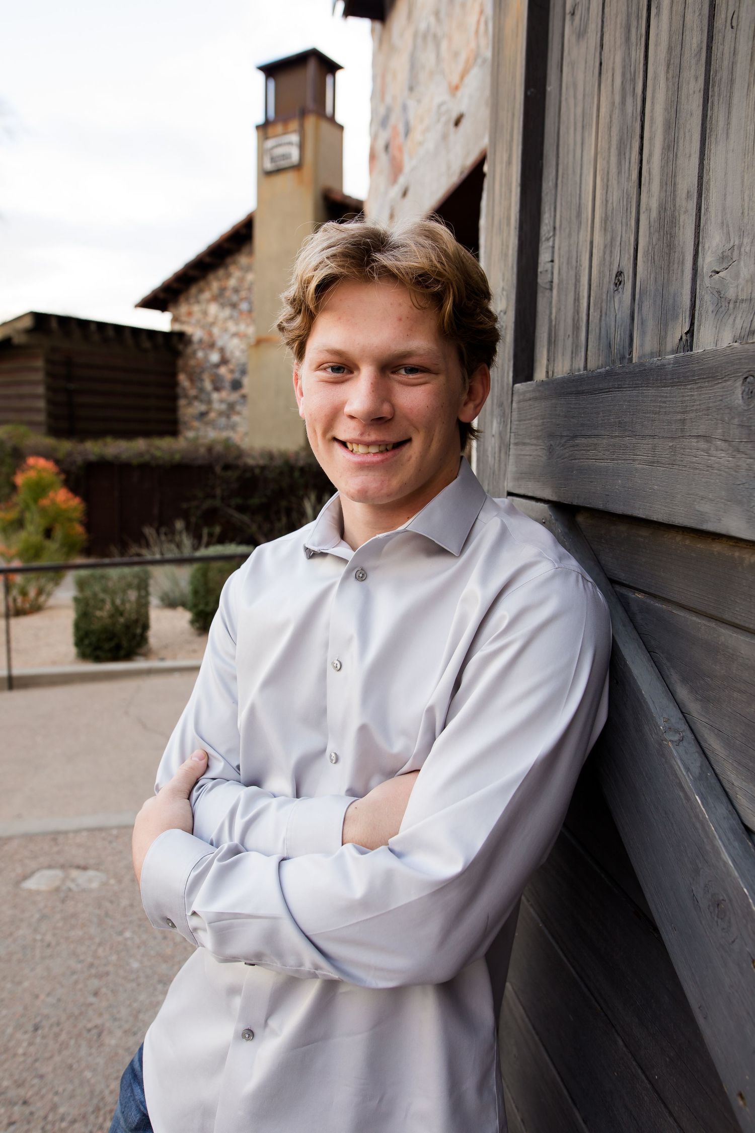 Senior graduate boy leans on a barn wood door and smiles at the camera for his Graduation portrait photoshoot session in Scottsdale.