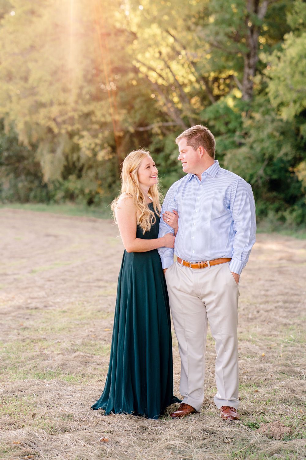 A romantic couple embraces outdoors during golden hour with forest scenery behind them.