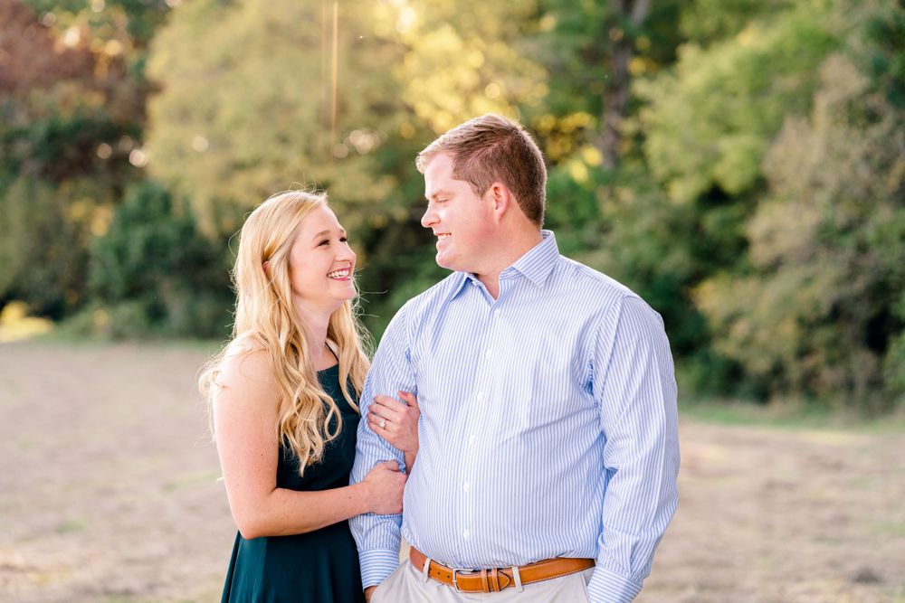A couple shares an intimate moment while standing in a sunlit field at sunset.