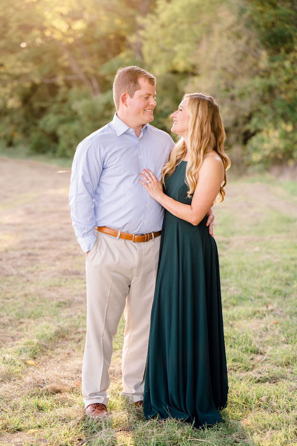 A couple in coordinated formal wear shares a loving moment in a grassy field at sunset.