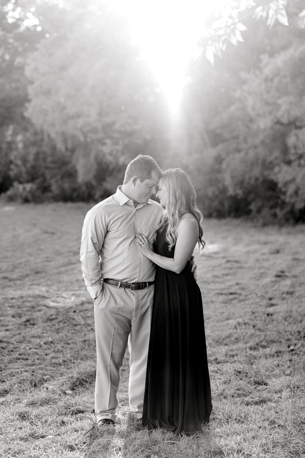 A black and white portrait of a couple in an intimate embrace with dramatic sunlight.