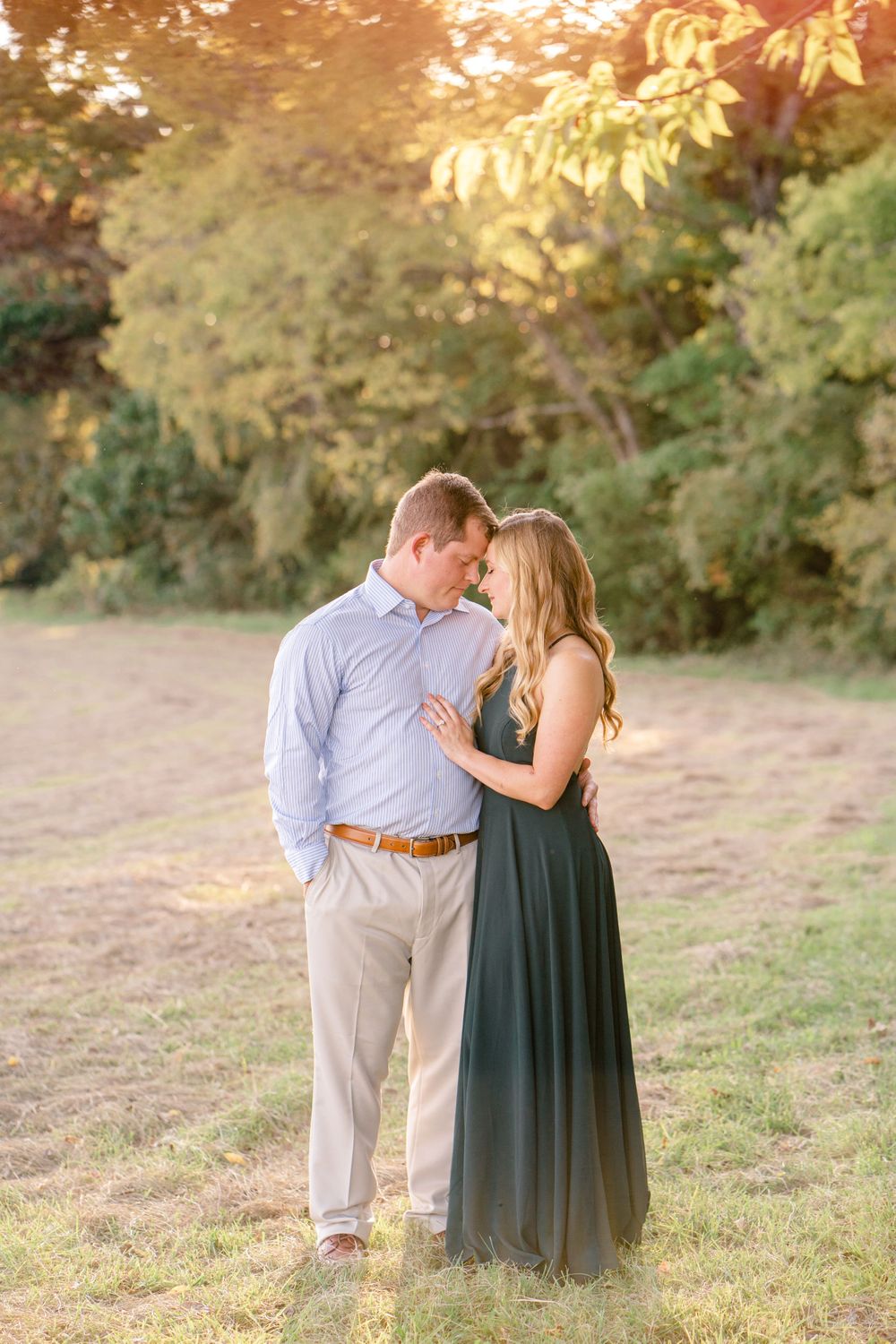 A couple in formal attire shares a romantic moment in a sun-drenched field.