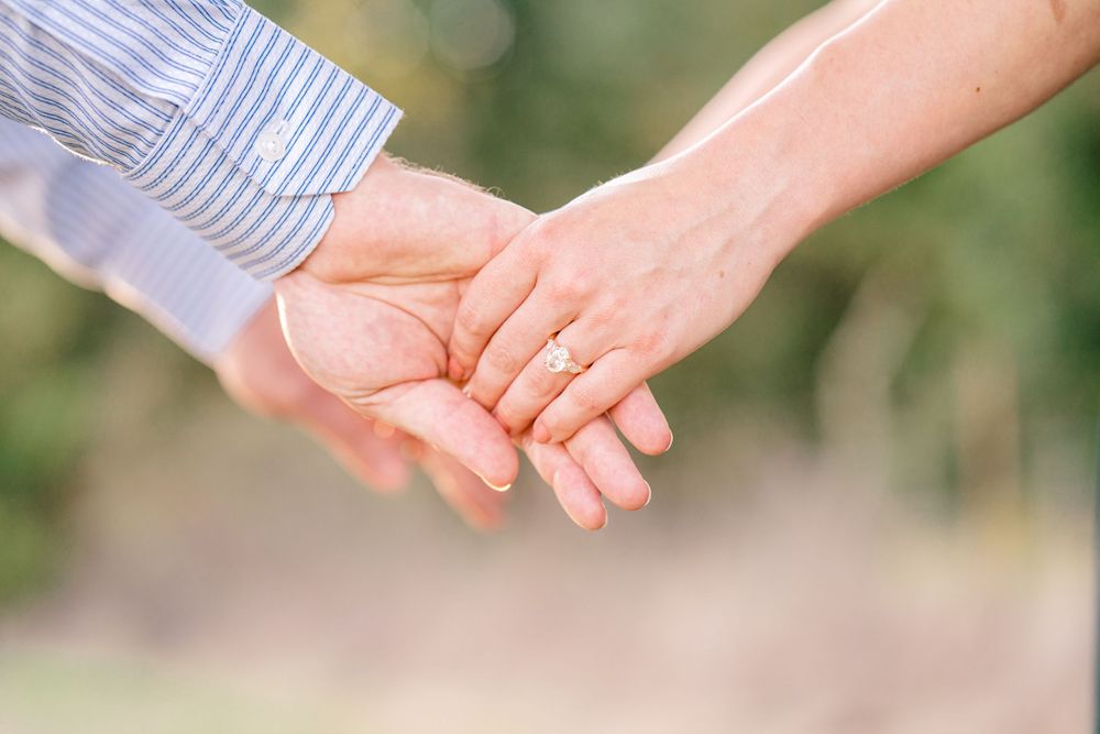 A close-up of two hands tenderly clasped together outdoors.
