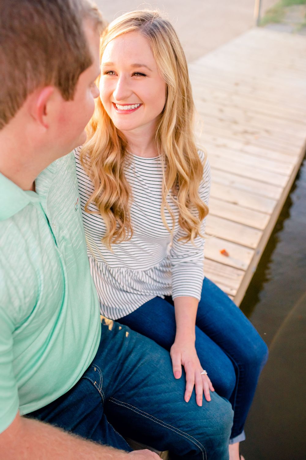 A couple shares a joyful moment while sitting together on a wooden dock by the water.
