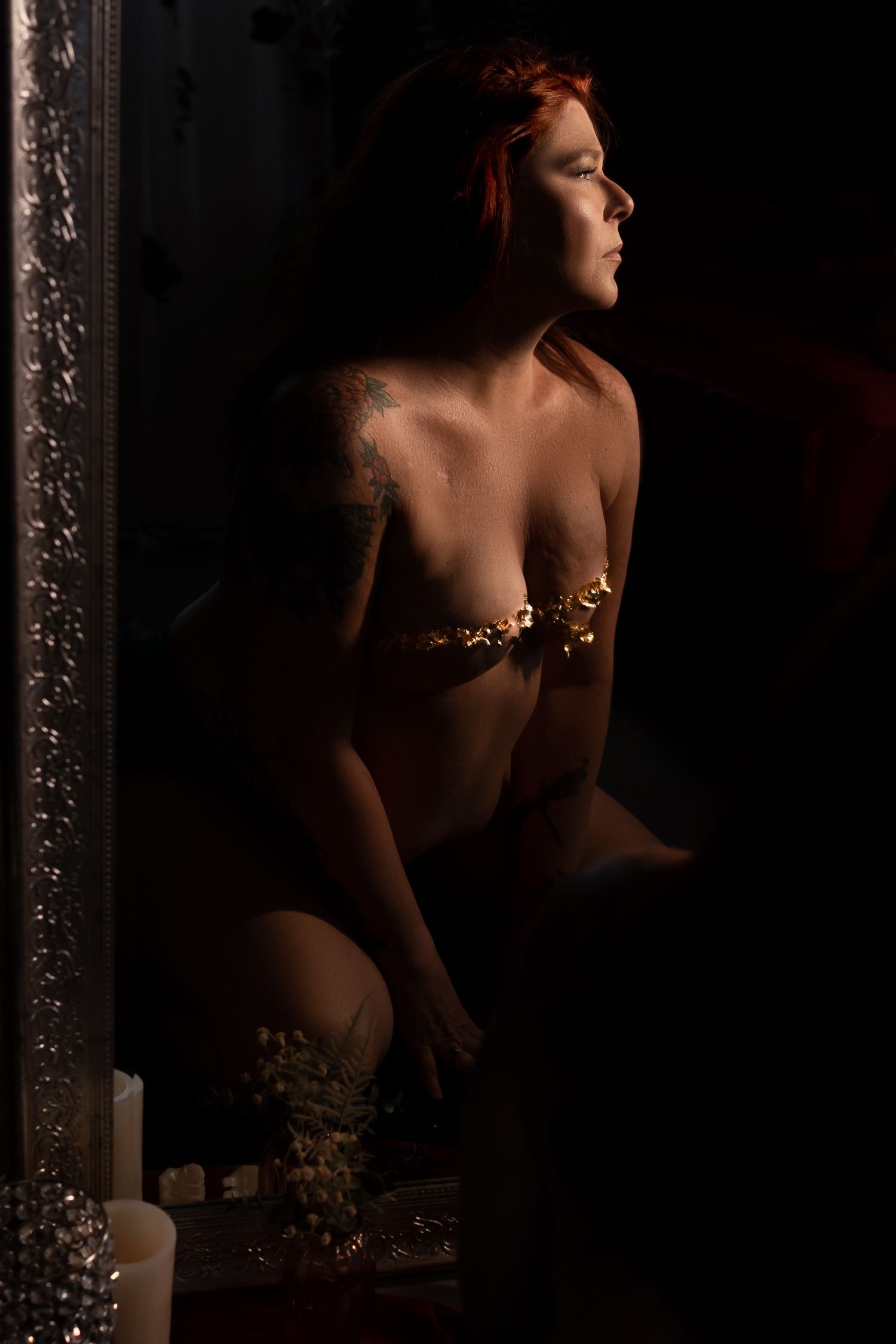 Artistic boudoir portrait with dramatic side lighting and ornate mirror frame.