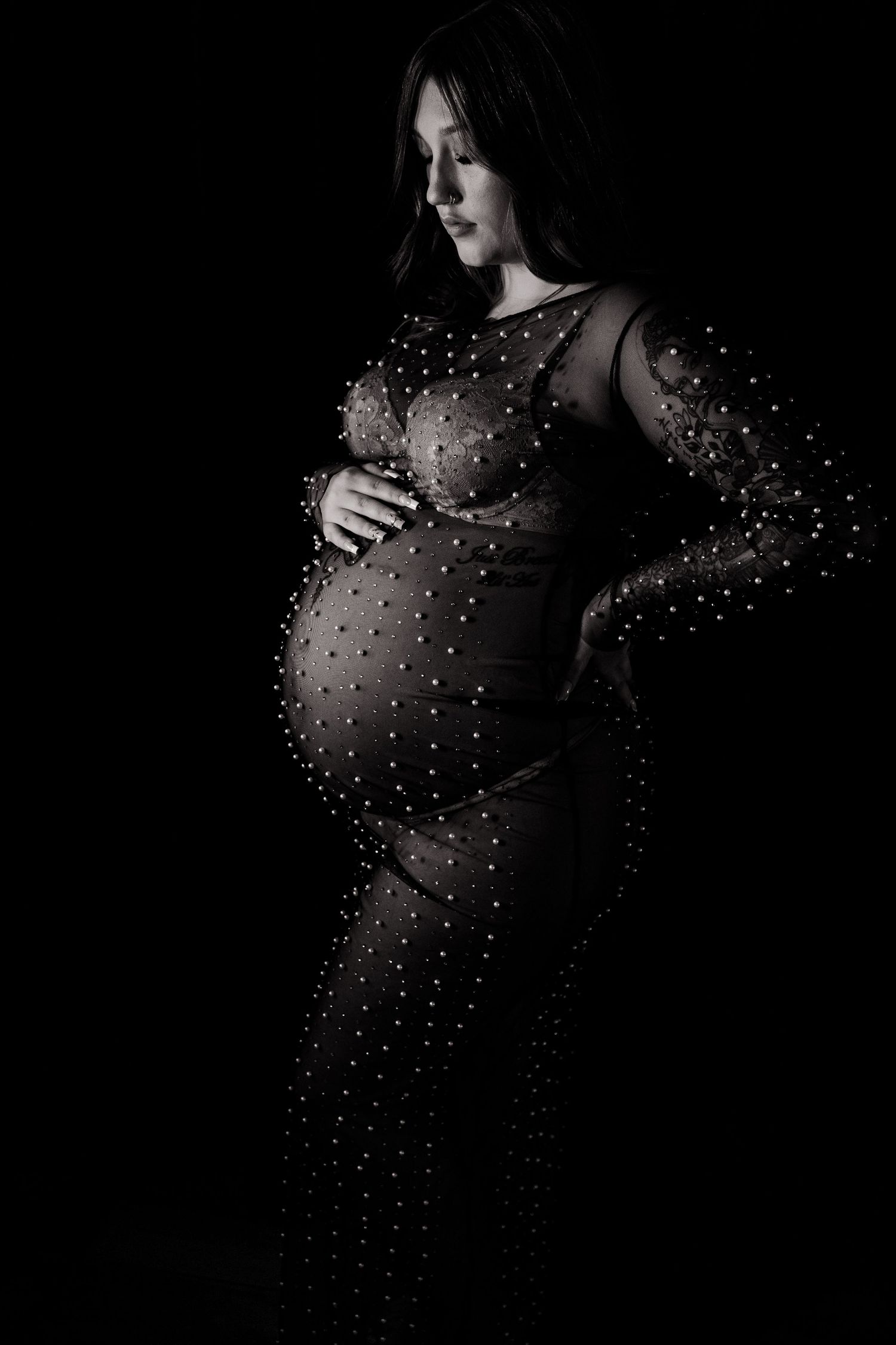 Elegant maternity portrait featuring a sparkly black dress against dark background.
